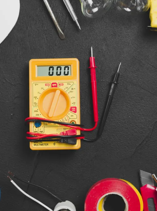 Multímetro y material eléctrico sobre una mesa de trabajo